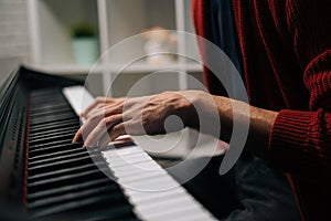 Close-up hands of unrecognizable musician man playing on synthesize gentle classical music at home.