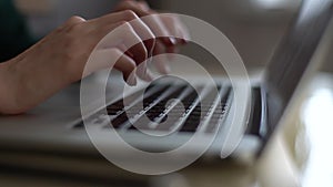 Close-up of hands of unrecognizable woman typing on laptop keyboard on background of window.