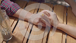 Close-up hands of unrecognized young guy and girl sitting outdoors at the table holding hands. Man and woman having date