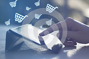 Close up of hands using digital tablet with abstract glowing cart icons on blurry background. Online shopping, e-commerce and
