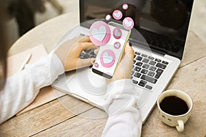 Close up of hands using smartphone with abstract hearts on blurry background with desktop, laptop and coffee cup. Likes, social