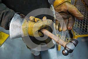 Close up of hands wearing protective gloves handling a hammer in a car factory photo