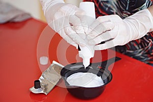 Close up hands wears gloves, squeezes dye hair color cream from tube in mix in black bowl before dying client\'s hair.