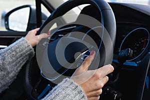 Close-up of the hands of a woman driving a car, holding the steering wheel with both hands. The woman has her nails painted red