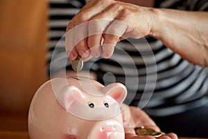 Close up hands of woman putting coin into piggy bank