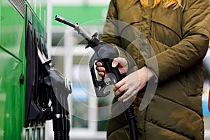 Close-up of hands of woman at self-service gas station, hold fuel nozzle and refuel the car with petrol, diesel, gas