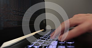 Close-up hands of woman sitting at desk, typing computer code on laptop keyboard, lines of digital symbols running on