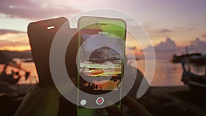 Close up of hands of woman taking video with mobile phone of sunset while sitting in the beach. 3840x2160, 4k