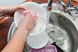 Close up hands of woman washing dishes in kitchen. Cleaning chores