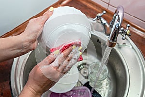 Close up hands of woman washing dishes in kitchen. Cleaning chores