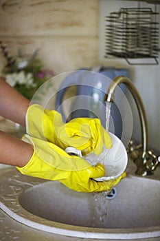 Close up hands of woman wearing yellow gloves washing dishes in kitchen