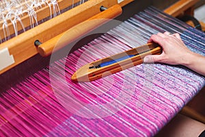 Close up hands of woman weaving purple and white pattern on loom