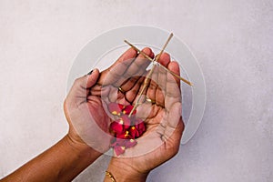 Close up of the hands of women holding a wood cross with red rose petals