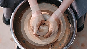 Close up of hands working clay on potter's wheel. Potter shapes the clay product with pottery tools on the