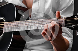 Close-up of hands of a young man playing guitar on a black background. Musical instrument, art concept.