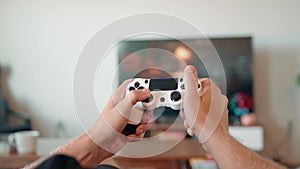 Close-up of the hands of a young man playing video games on a game console in front of a widescreen TV