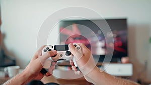 Close-up of the hands of a young man playing video games on a game console in front of a widescreen TV