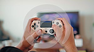 Close-up of the hands of a young man playing video games on a game console in front of a widescreen TV