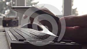 Close up on hands of young man using tablet while sitting computer keyboard and mouse. Freelancer photographer working