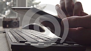 Close up on hands of young man using tablet while sitting computer keyboard and mouse. Freelancer photographer working