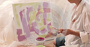 Close-up of hands of young woman artist in a white shirt painting picture in art studio.