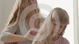 Close-up hands of young woman combing hair of her blond daughter. Concept of motherhood, childhood, one parent. Leisure