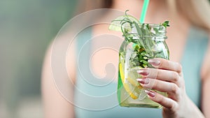Close-up hands of young woman giving refreshment healthy cocktail with slice of lemon and mint