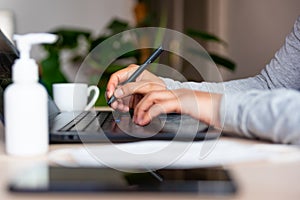 Close up of hands of young woman typing on laptop keyboard with hand sanitizer while remote working due to corona virus spread photo