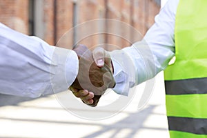 Close up of handshake between caucasian architect and african american engineer during work at outdoors construction