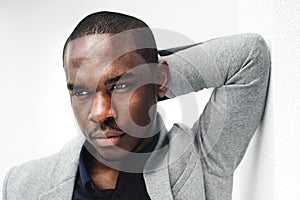 Close up handsome african american man leaning against wall with hand behind head and looking away