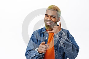 Close up of handsome Black man points at you, shows telephone, phone call gesture, give me your number gesture, stands