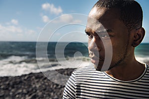 Close up handsome black man standing by water staring