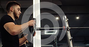 Close up of handsome bodybuilder guy prepare to do exercises with barbell in a gym, keep barbell plate in hands. High