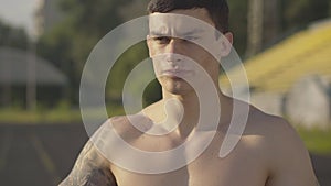 Close-up of handsome brunette sportsman drinking water and leaving. Portrait of serious Caucasian man training in summer