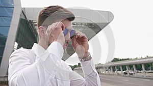 Close-up of handsome fashion male model taking on his sunglasses and looks to the camera. Urban city background