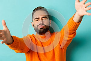 Close-up of handsome happy man reaching hands forward, stretching arms for hug and kiss, standing against turquoise