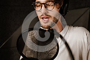 Close up handsome male musician in headphones sensually singing in microphone in modern sound recording studio