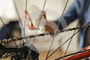 Close up of handsome man in casual clothing lubricate the bike chain with oil at home