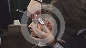 Close up of a handsome man getting shaved with a razor by a barber