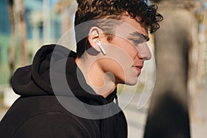 Close up handsome man listening music in wireless earphones. Attractive guy resting after workout outdoor