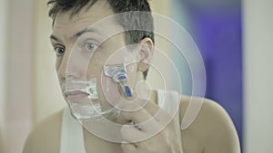 Close up. Handsome man looking at mirror and shaving in bathroom.