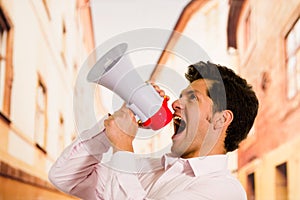 Close up of a handsome man screaming with a megaphone, pointing to the sky in a blurred background