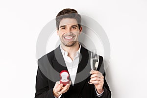 Close-up of handsome man in suit, making a proposal, giving engagement ring and raising glass of champagne, standing