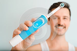 Close-up of handsome man with white toothy smile showing electric toothbrush, advertisement. Selective focus on modern device