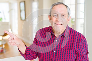 Close up of handsome senior man at home with a big smile on face, pointing with hand and finger to the side looking at the camera