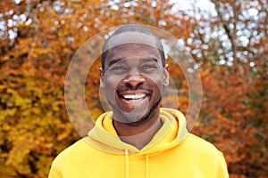 Close up handsome young black man smiling against autumn leaves in background