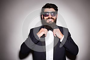 Close-up of handsome young man wearing sunglasses adjusting his bow tie and looking at camera