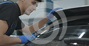 Close-up of handsome young service man cleaning windshield of vehicle. Portrait of professional Caucasian repair shop