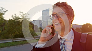 CLOSE UP: Handsome yuppie talking on phone while walking through city at sunset.