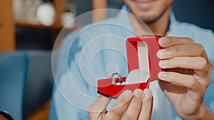 Close up happy asian couple man and woman smiling boyfriend sit on couch surprise girlfriend with engagement ring in red box ask